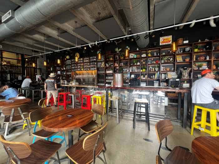 Veza Sur micro brewery and bar in Wynwood, with a big venue with a mix of colorful and wooden furniture, and a dark colored bar with all the drinks on a long shelf behind the bar