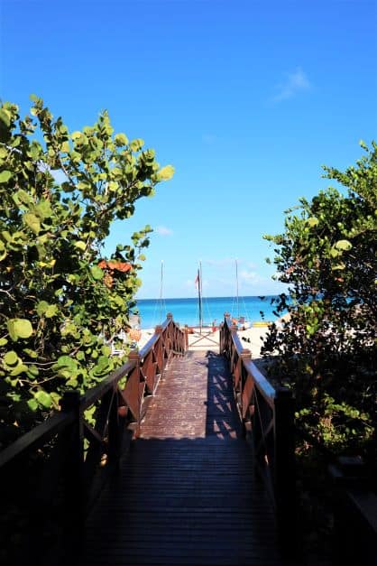 Brown wooden walkway to exit from the Varadero dive center to the beach. You see the beach and the sea at the other end of the walkway, warm white sands and blue seas and sky. 