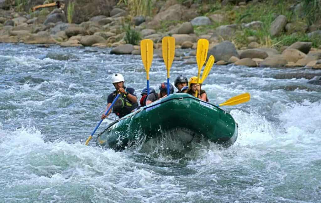 Whitewater rafting on a fierce river in Costa Rica; a green raft with a paddle crew inside with helmets on maneuvering down the white chappy river