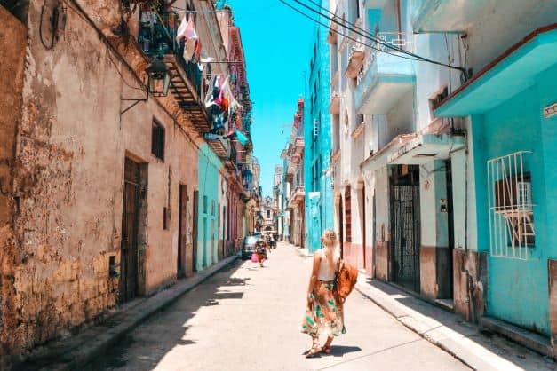 Tourist waking the streets of Old Havana between colorful but run-down houses on a bright sunny summer day. 
