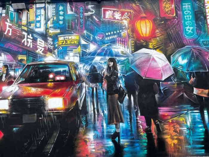 Art piece in Wynwood Walls, a dark colorful painting from an Asian street scene with lots of cars, people, lights, on a dark rainy night. People walk with umbrellas 