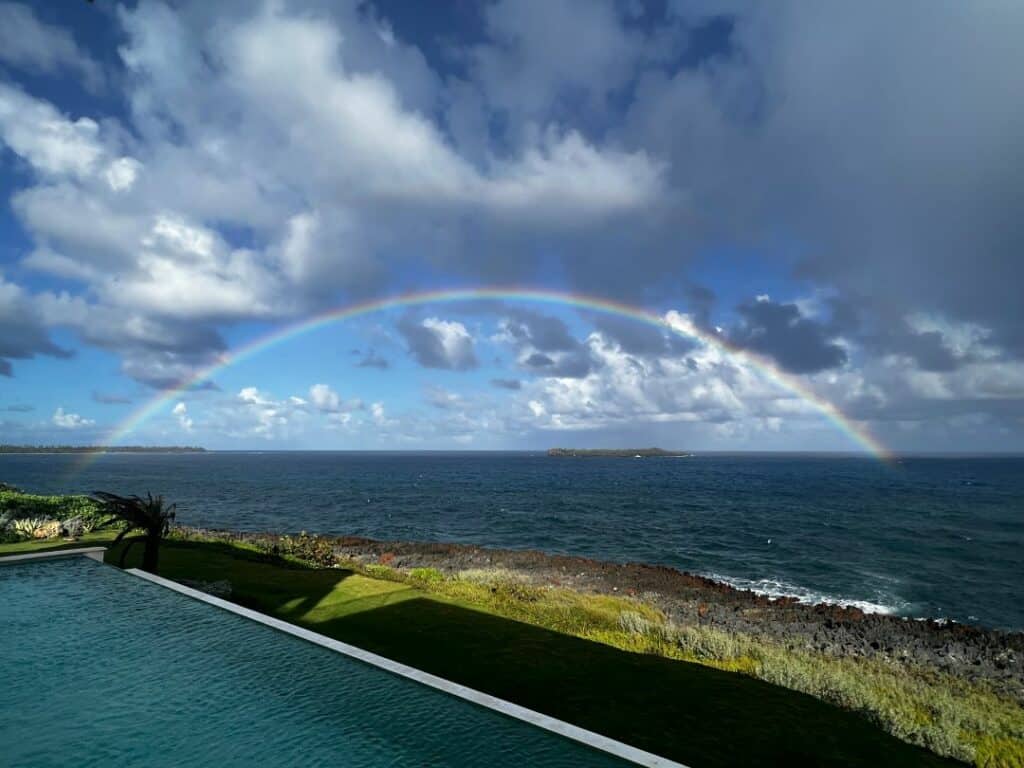 A beautiful rainbow over the dark ocean outside the northern shores of Samana peninsula, from a mansion where you see the pool in the lower frame of the photo under a partly blue sky. 