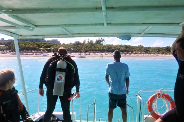 Heading out scuba diving in Varadero Cuba. View towards the beach at the aft of the boat, with a diver ready to jump into the light blue sea. 