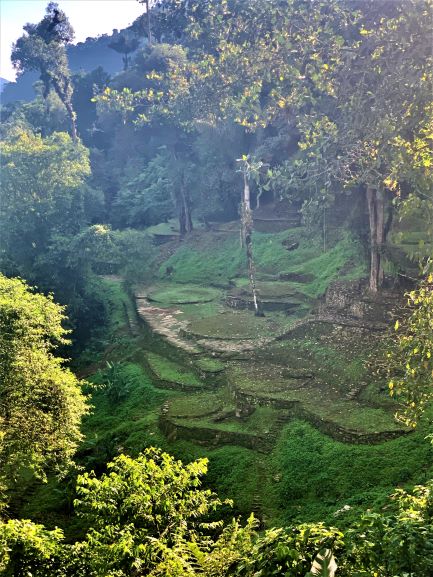 A side area to the main part of the Lost City, with lots of circular ruins in the green grass, surrounded by hilly green forest. 