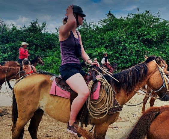 Horseback riding outside Trinidad Cuba, a woman on a horse holding on to her helmet, waiting to get going, lots of green bushes along the path 