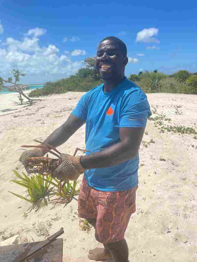 A locan man holding a fresh lobster, that is going to be prepared on a BBQ right on the white sandy beach in the sunshine