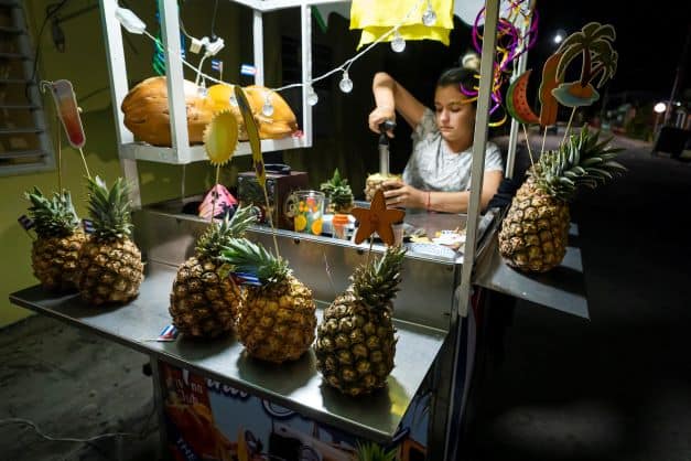 Local girl serving pina colada cocktails from a wagon in Varadero Cuba at night served in pineapples. 