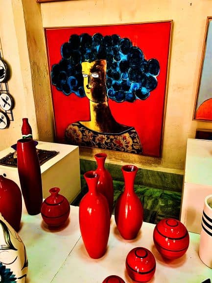 A large red painting of a woman in Gallery Forma in Obispo Street in Havana, in an eclectic rough style. A table with bright red decorative vases. 