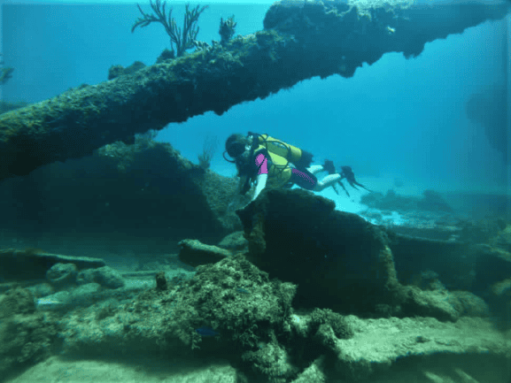 Swomming next to a small wreck, crystal clear waters, and wearing a yellow and pink wet suit with a yellow tank. 
