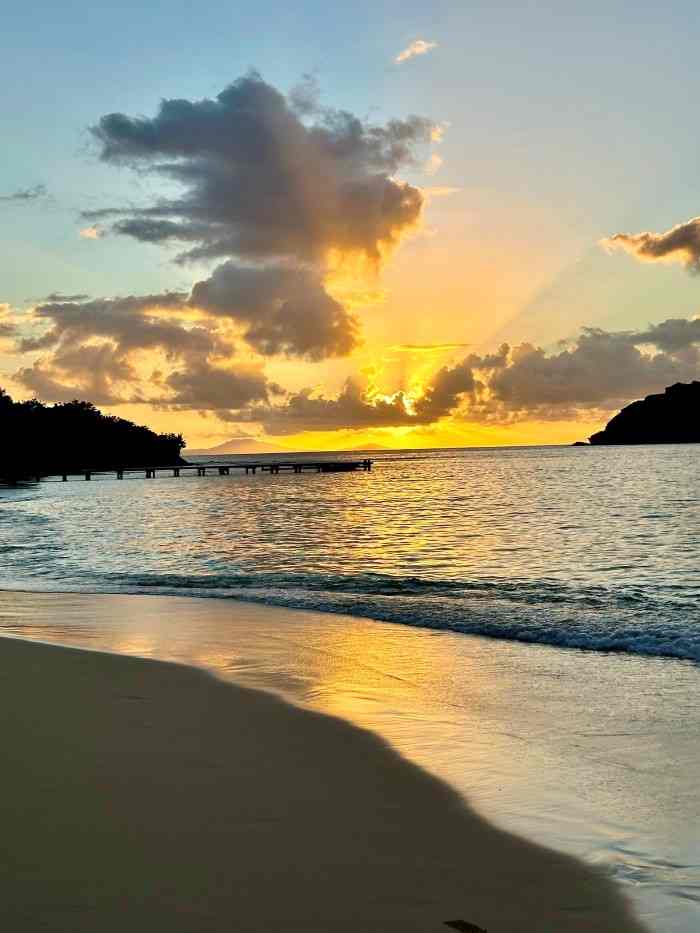 Sunset on the golden sandy beach, the sunset reflecting in the water and all over the golden sky in the distance