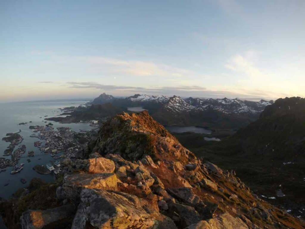 Stunning views from a mountain top above Svolvær in Lofoten, with the small town below, and vat mountains and the sea in the distance under a pale blue sky