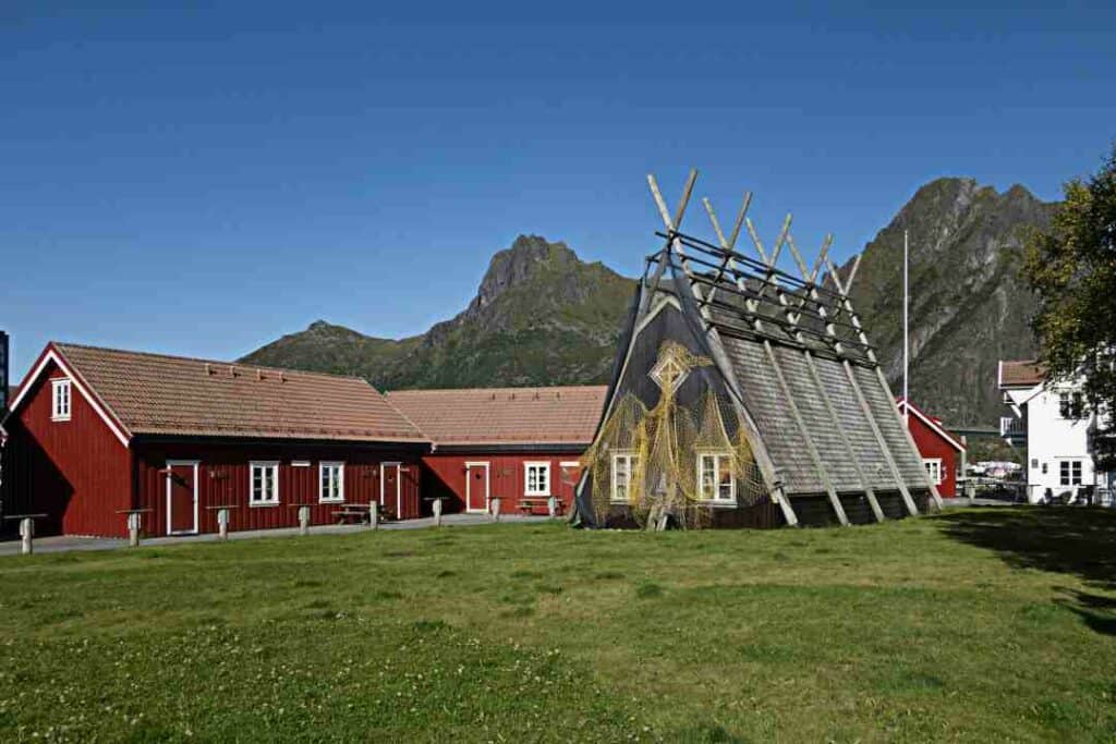 Svolvær on a summer day, with green grass and red traditional wooden houses, under the vast mountains and the blue sky