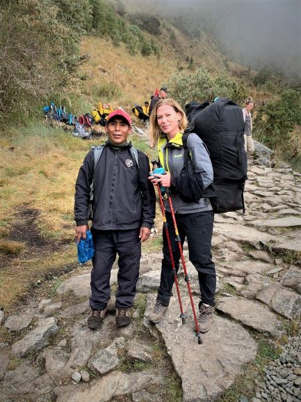 Solo travel to Peru: hiking the Inca Trail: I am standing smiling next to the sherpa wearing the sherpa backpack, smiling after finishing the sherpa challenge (which is carrying the sherpa backpack uphill for half an hour)