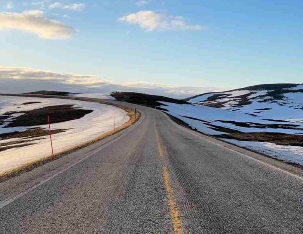 The road to the North Cape in Norway, a long stretch across mountain plains on the Magerøya island on a spring day with blue skies, and still patchy snow on either side of the road