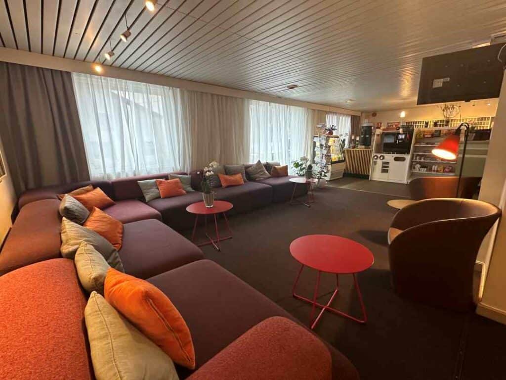 The foyer at Scandic Honningsvåg hotel, with colorful pillows in the big sofas, round red tables, and a small shop area