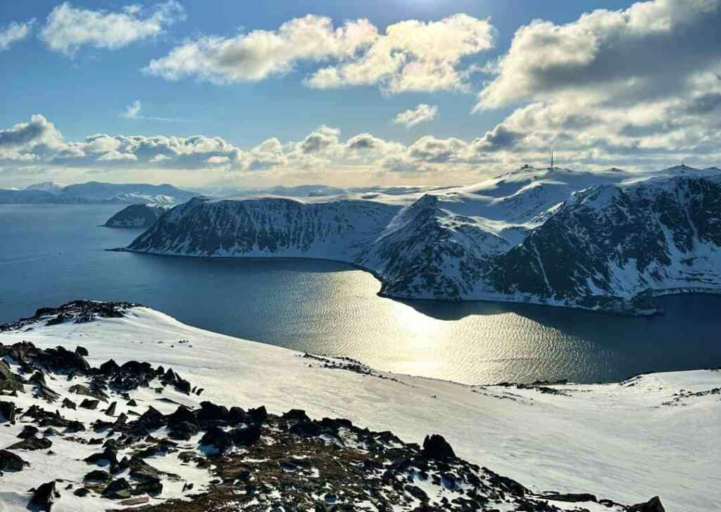 From the top of the Sherpa Stairs in Honningsvåg, stunning views from the partly snow-covered mountain over the blank fjords and snow-covered mountain plains in the distance under blue skies with brilliant sunlight