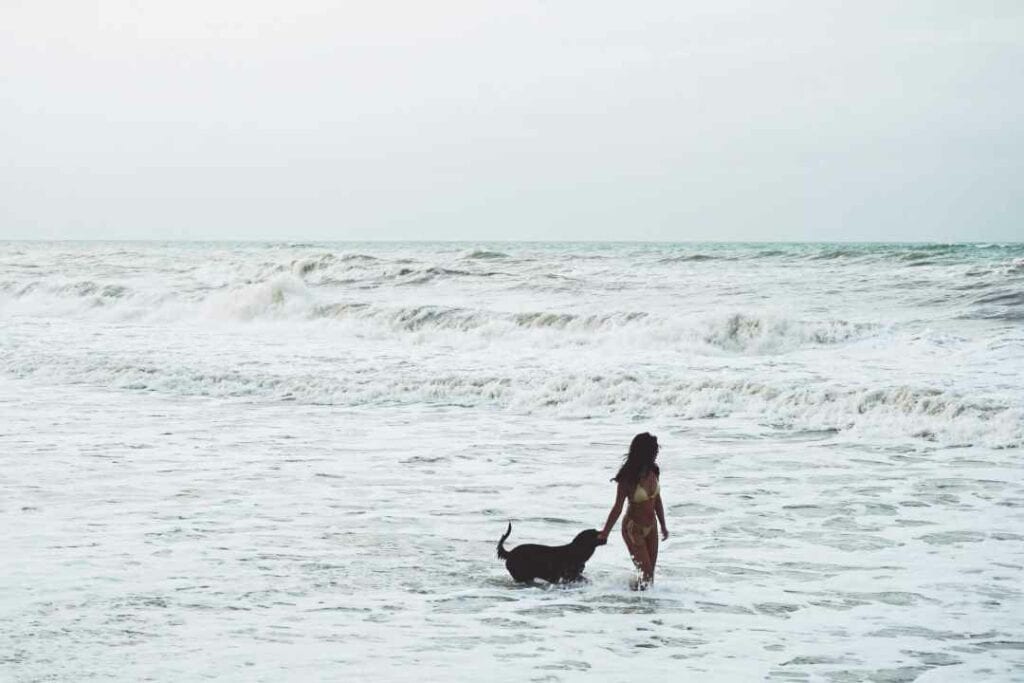 Woman walking with her dog in the whitewater on a beach in Colombia