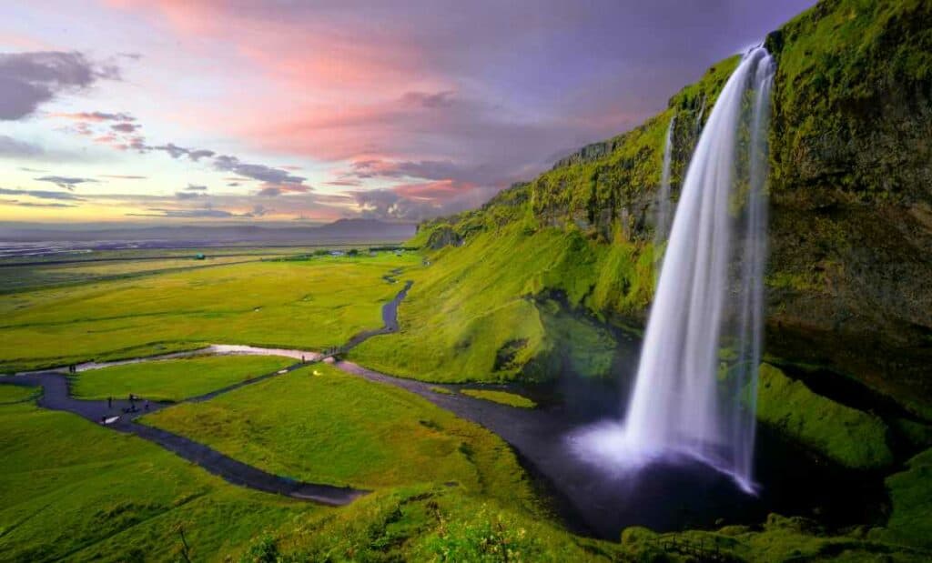 Incredible green planes around the spectacular Seljalandsfoss Waterfall in Iceland with the setting sun making the sky pink in the background