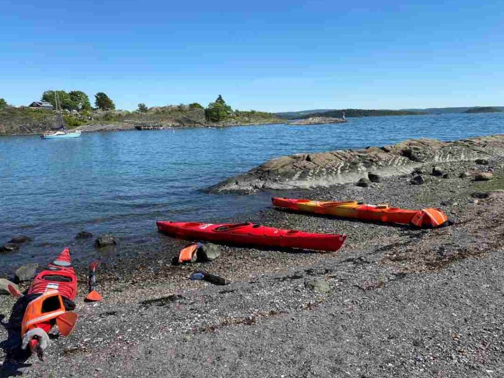 Three kayaks lying on a stone beach next to dark blue waters under blue skies on a summer day