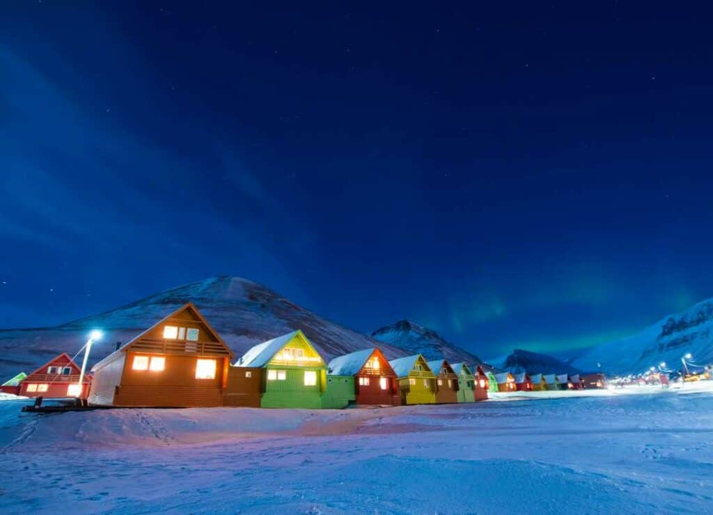 Winder in Svalbard, north of Norway, with a dark blue sky, bluish snow, and colorful houses lit by warm lighting