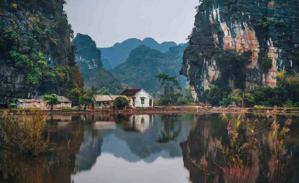 Beautiful landscape by a lake in northern Vietnam, where old wooden houses are reflected in the blank water in front of the lust green covered mountain sides