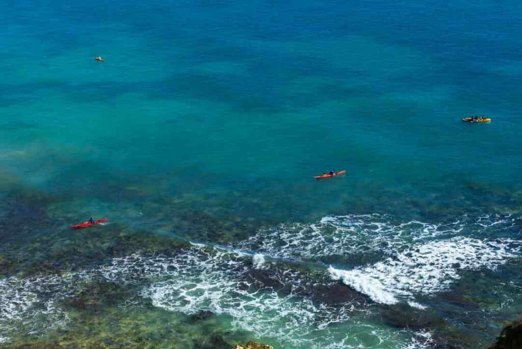 The beautiful rugged coastline of Algarve, Portugal, with greenish water and three canoers slowly paddling the water