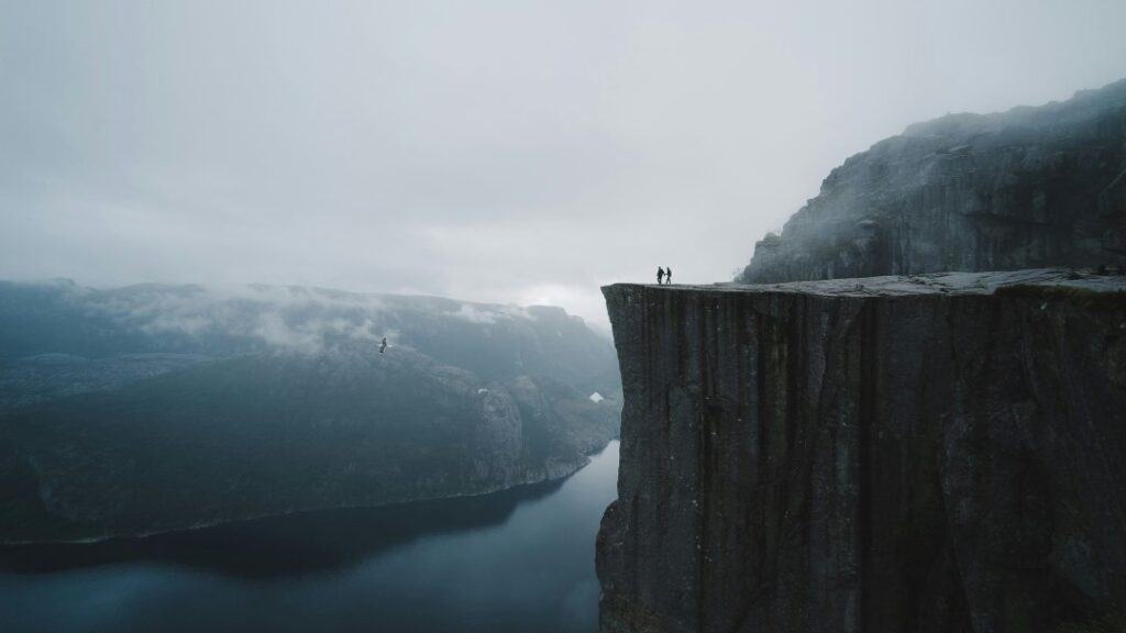 A spectacular viewpoint on top of a mountain ledge where the mountain sides go straight down to the fjord hundreds of meters below under a misty sky