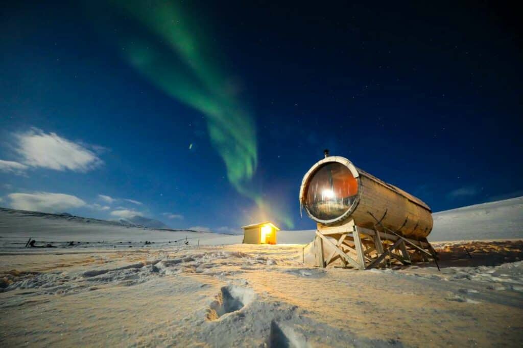 A frozen Arctic winter night in Svalbard with a dark blue sky over the white snow where the Aurora Borealis is dancing across the sky in greens