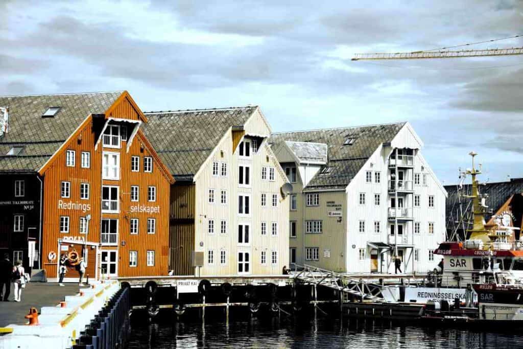 Charming old wooden houses in different colors by the dock, a boat on the water in front of the dock under a dotted cloudy sky