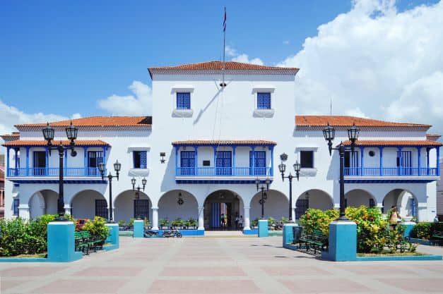 The white town hall with red roof and blue details on the balcony with a large yard in front on a sunny day