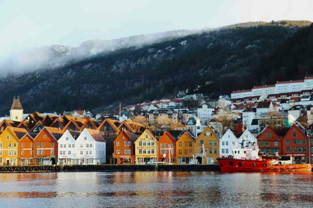 Bergen Brygge, the wharf, on a cold clear winter day, with the colorful houses surrounding teh harbor, boats docked at the shore, and the mountains in the background slightly covered in snow and a bit of fog