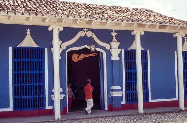 The blue and white decorated Casa de la Trova in Santiago de Cuba, with a man in the entrance, and cobblestoned streets on the outside