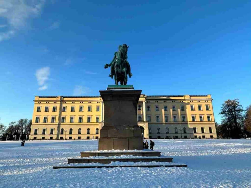 The yellow Norwegian Royal Palace in Oslo in Winter with the huge statue in front under a deep blue sky