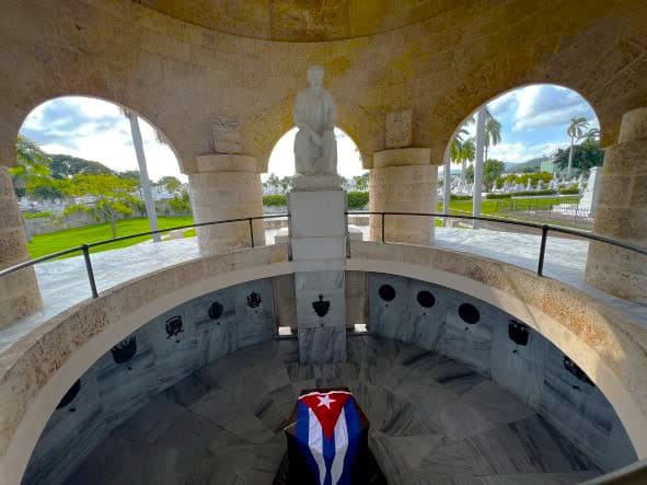 Jose Marti Mausoleum at Ifigenia Cemetary in Santiago de Cuba, his coffin lowered in an open structure surrounded by grey marble under a beautiful white and yellow stone dome, the cemetary can be seen in the background through open arch windows