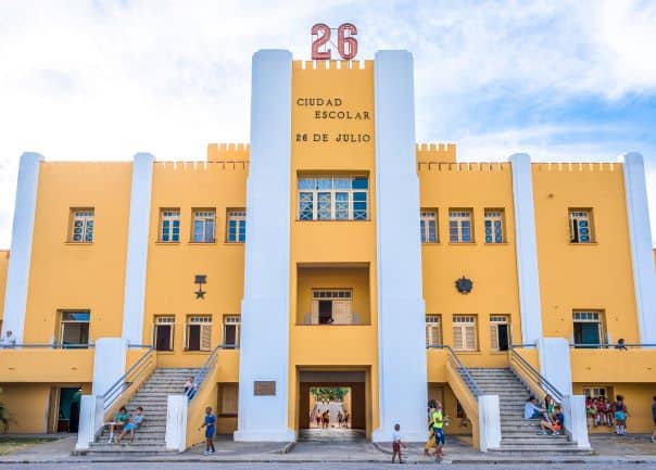 The modest yellow and white facade of the Moncada barracks in Santiago de Cuba with two wide stairways going up to the main entrane on a sunny summer day