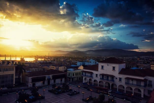 The square Parque Cespedes in Santiago de Cuba at sunset, with lights in the aquare surrounded by colonial architecture buildings in white and wood