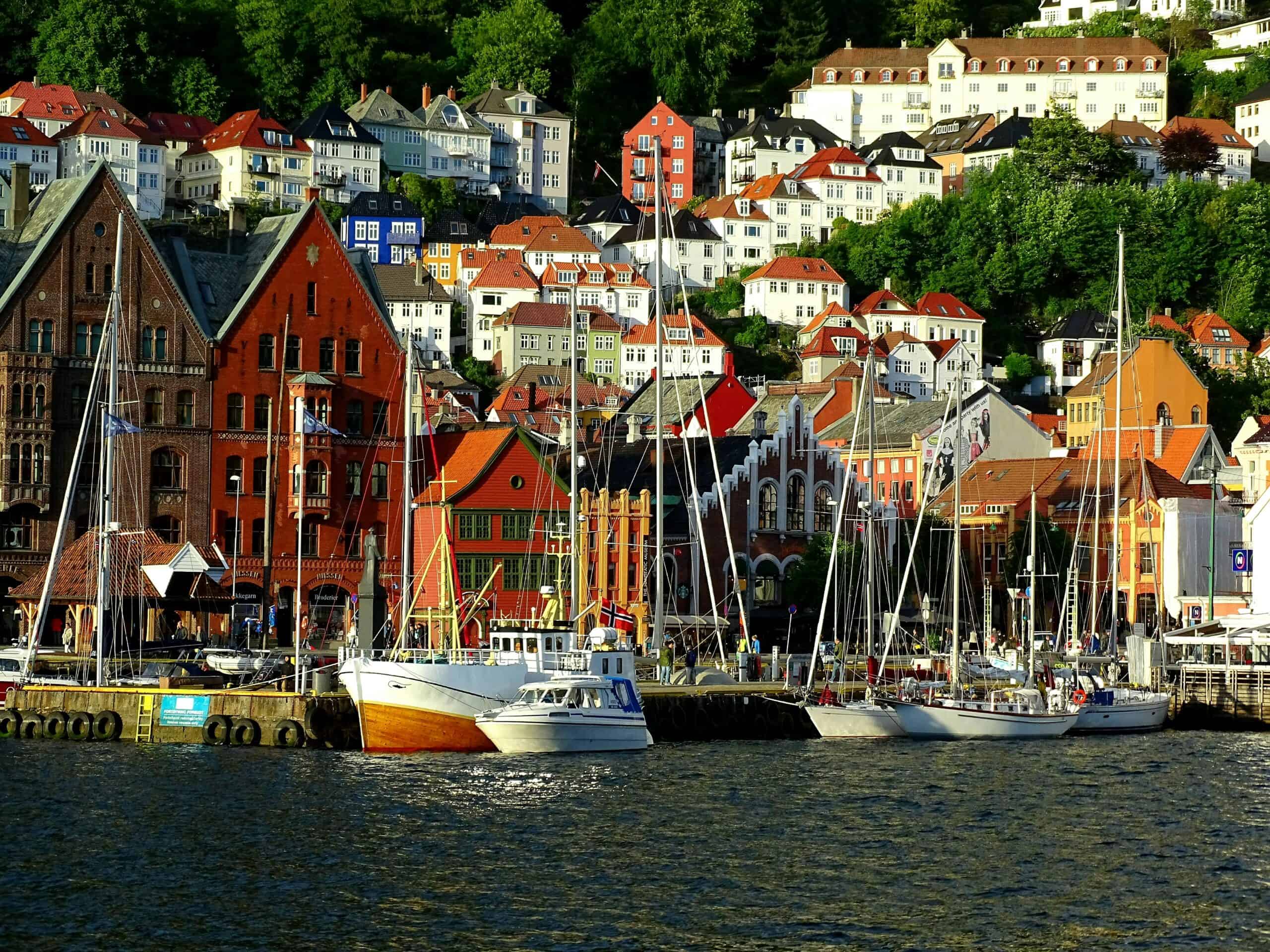 Summer in Bergen Norway, with the colorful houses along the Bergen Wharf, many fishing boats docked along the port, and charming white houses in the background on a sunny day