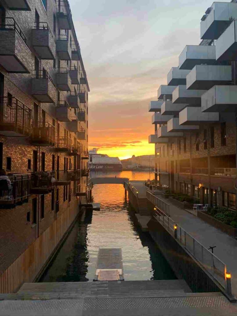 Sunset over Sørenga in Oslo, the golden sun in the horizon reflected in the water between the modern buildings