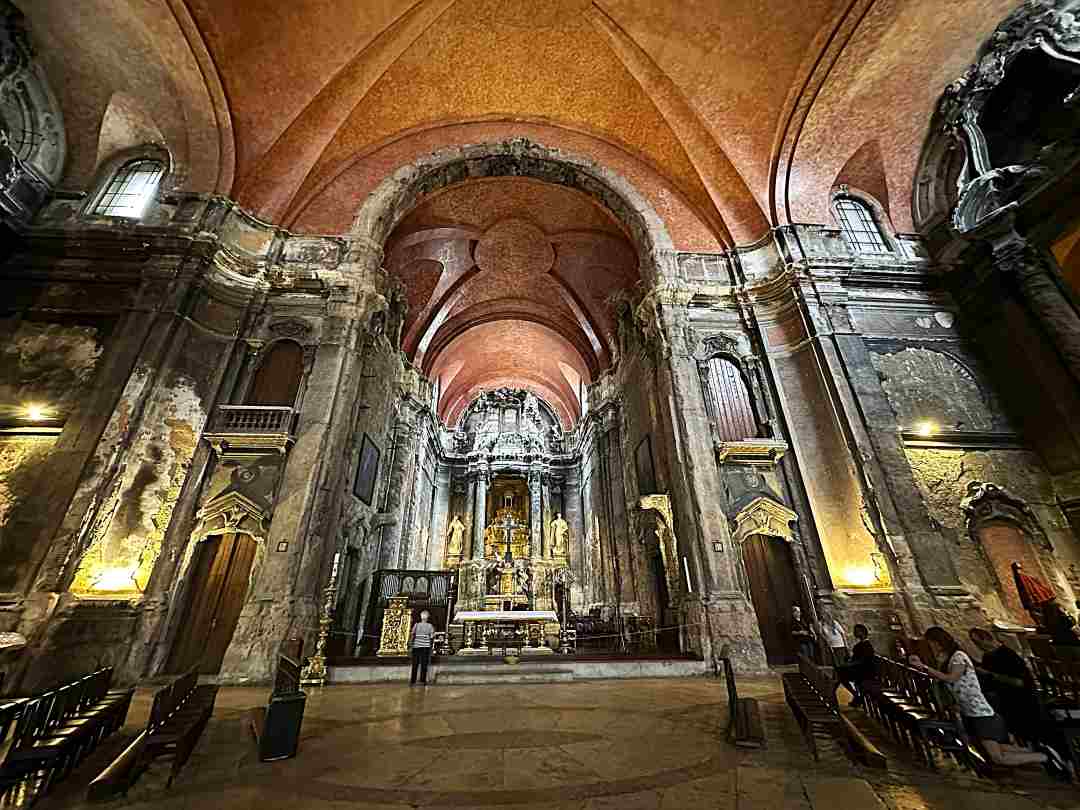 The stunning interior of a cathedral with high ceilings, incredible artwork, and colorful details in red and gold.