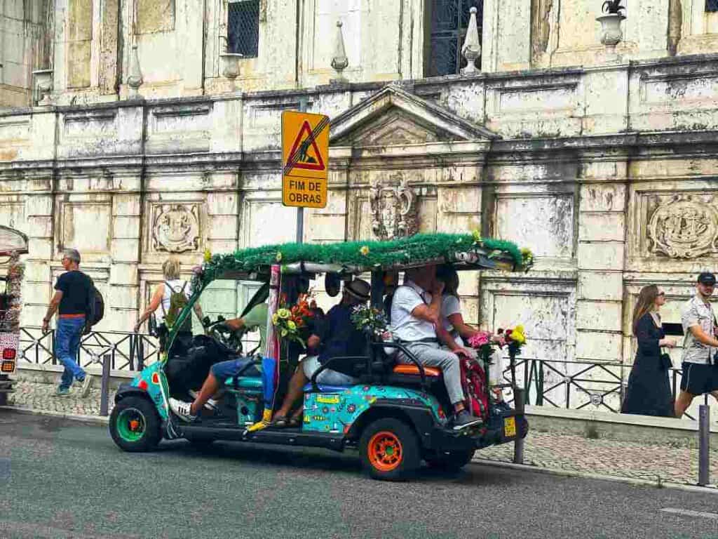 A colorful tuktuk car painted with many colors with a grass roof, and people enjoying the ride of a city