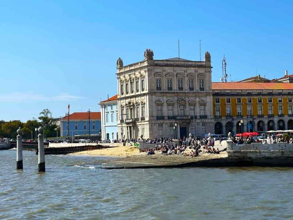 A stone stair tilting into the water, people relaxing on the stairs against the city scape in the background on a sunny day with blues skies