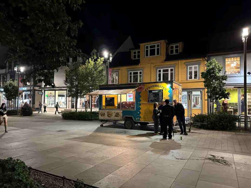 A town street at night with a food truck, lights from stores and street lights, and people enjoying the night town  