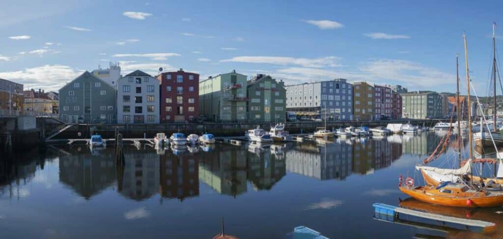 A harbor area with dark blank waters, boats docked at the jetty, and charming colorful houses under a blue sky