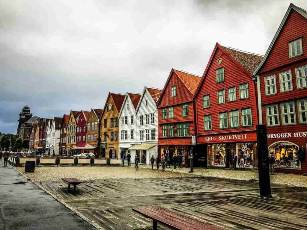 A charming wide wooden and stone jetty area on a rainy day, with old charming wooden colorful houses lining the space under a cloudy sky.  