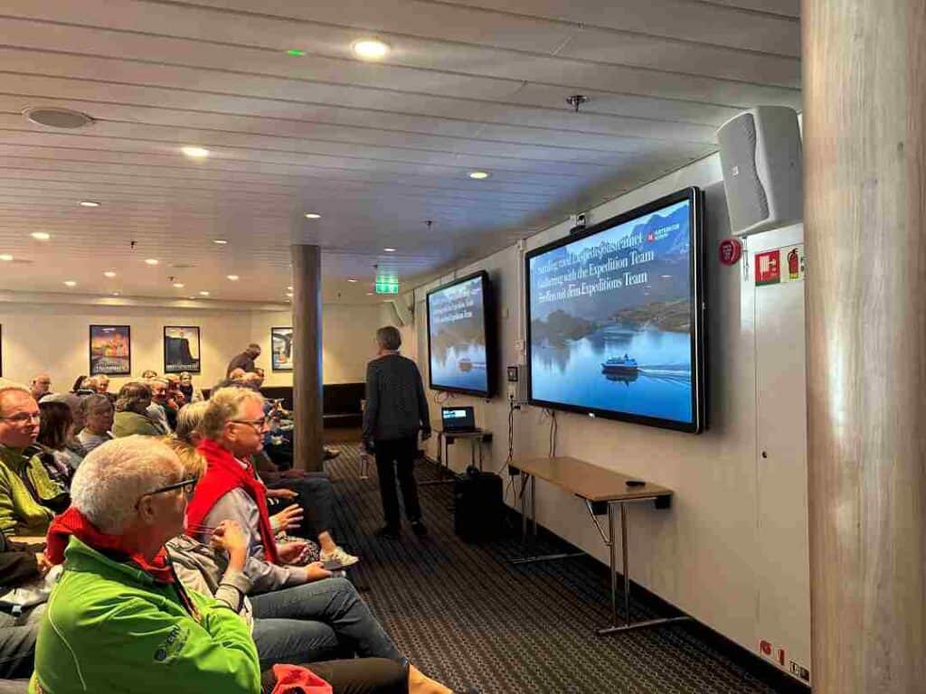 People seated in a conferance room inside a ship ready for a talk about the Norwegian coastline