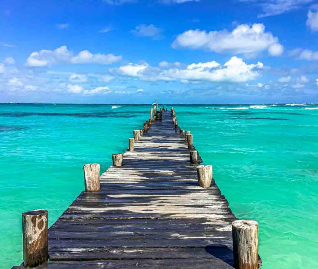 A wooden pier stretching out over the greenish blue paradisiacal waters under a blue sky