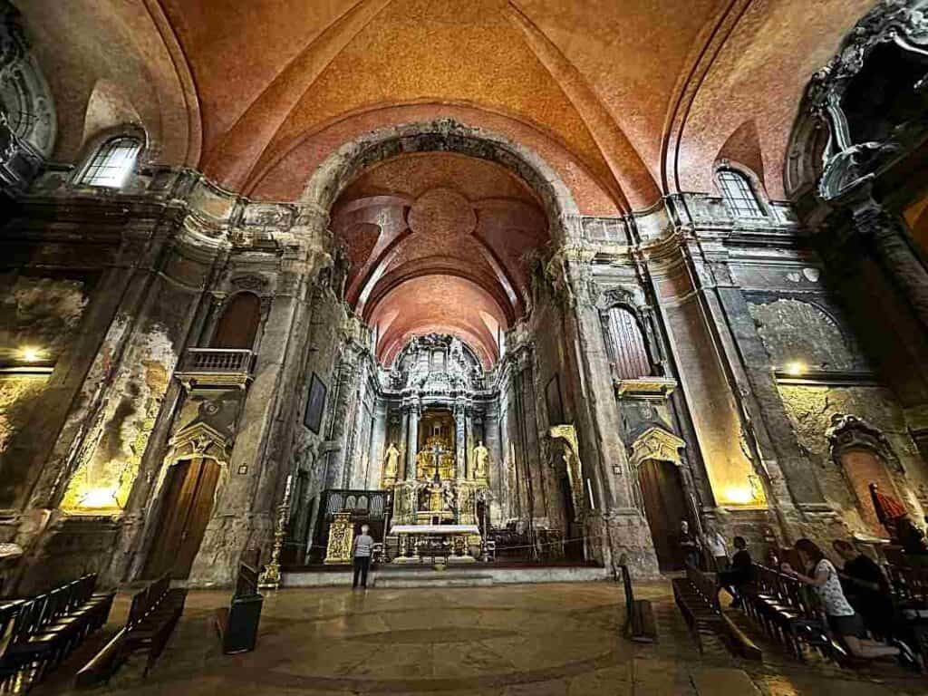 The incredible interior of a cathedral with golden lighting, high arched ceiling, colunms and exquisite details, artwork evertwhere and a majestic altar at the end