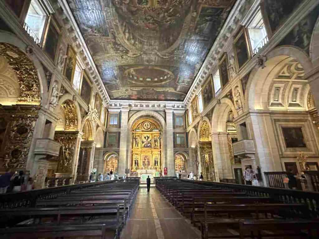 The aile inside a stunning cathedral with seat rows on each side, and a vast high ceiling, wihte marble, artwork, golden lighting and stunning details 