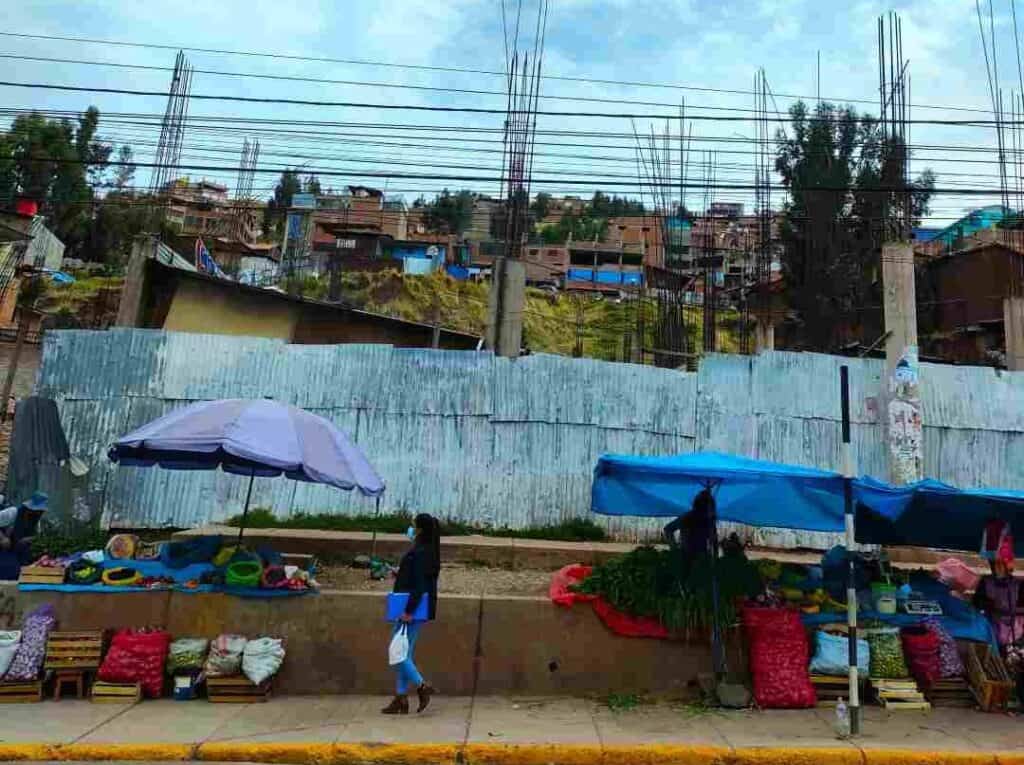 A city scape of a rugged part of a city with improvised market stalls where people sell vegetables and spices below a scruffy residential area