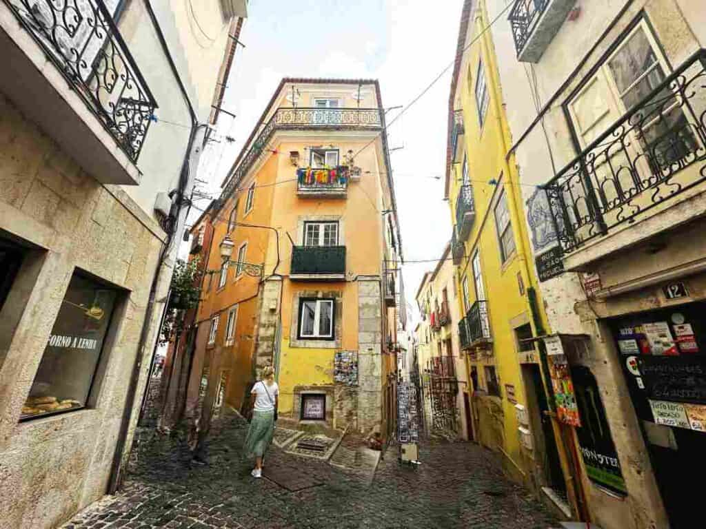 A narrow street with cobblestones, surrounded by tall colonial old buildings in stone, with lots of different doors and windows in grey and yellow, a charming view